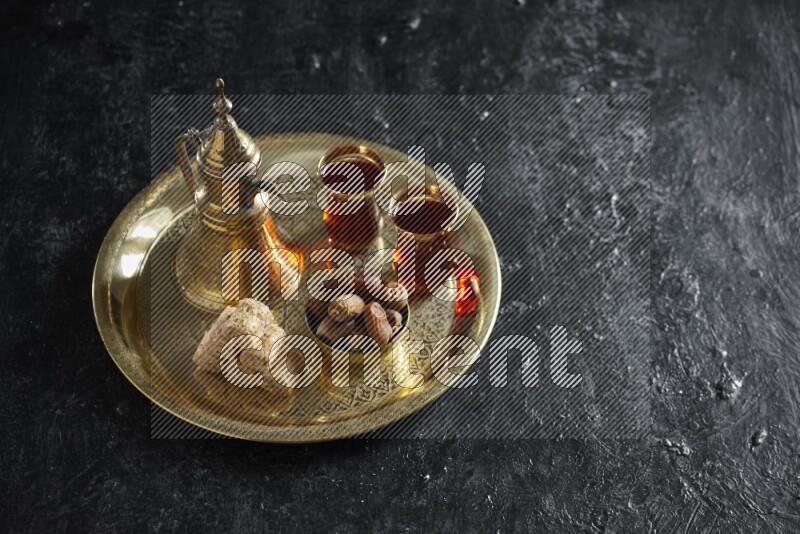 Oriental sweets with dates and a drink on a metal tray in a dark setup