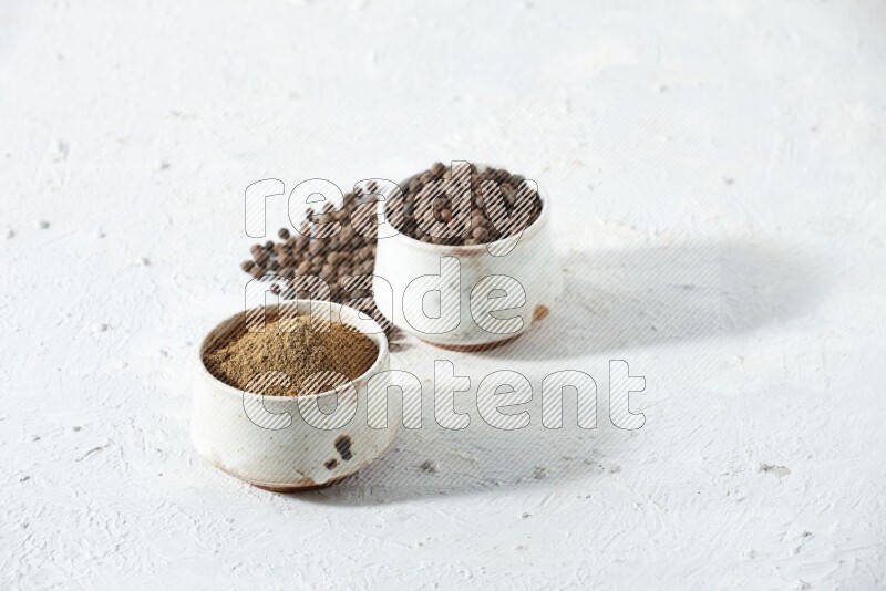 وعاءان بيج، أحدهما ممتلئ ببودرة بهار الفلفل الحلو والآخر بالحبوب مع البودرة والحبوب متناثرة على خلفية بيضاء