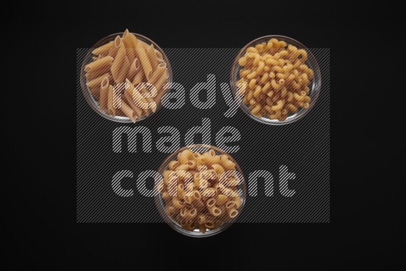 Different pasta types in glass bowls on black background