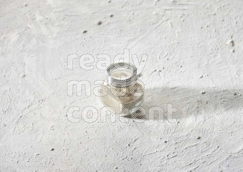 Herbal Glass jar full of white pepper powder on textured white flooring