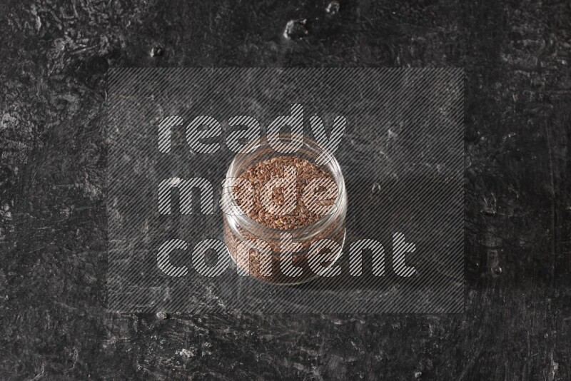 وعاء زجاجي ممتلئ بحبوب بذر الكتان علي خلفية سوداء