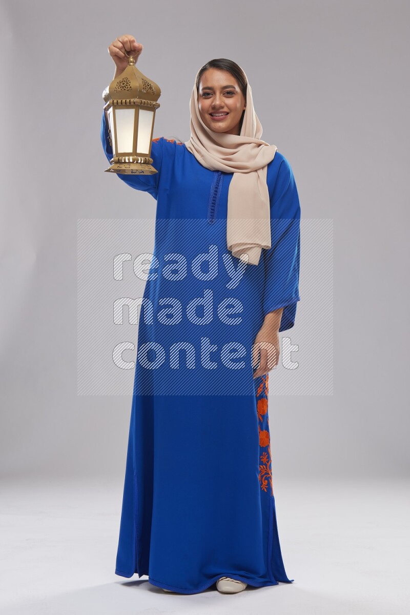 A Saudi woman standing wearing Jalabeya holding a lantern