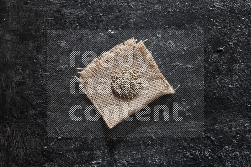 White pepper beads on a burlap piece of fabric on textured black flooring