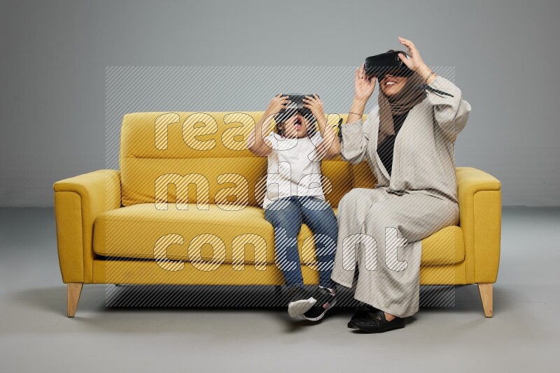 A girl and her mother sitting playing with VR on gray background