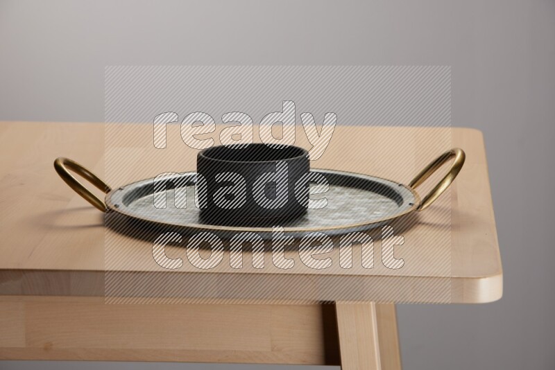 black bowl placed on a rounded stainless steel tray with golden handels on the edge of wooden table