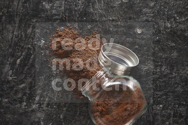 وعاء زجاجي للتوابل مقلوب ممتلئ ببودرة القرنفل والبودرة سقطت منه على أرضية سوداء