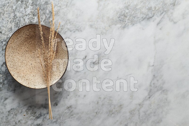 Wheat stalks on multicolored pottery plate on grey marble background