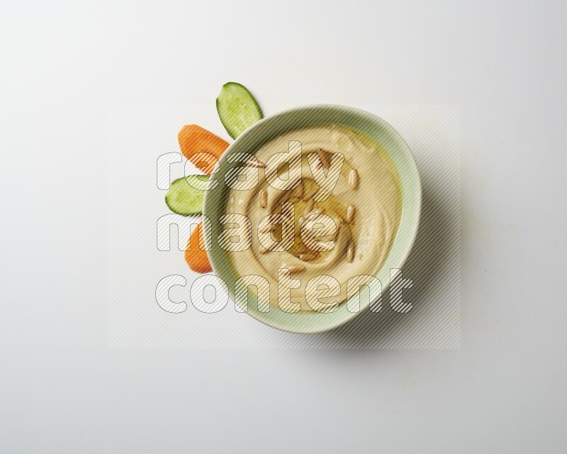 Hummus in a green plate garnished with pine nuts on a white background