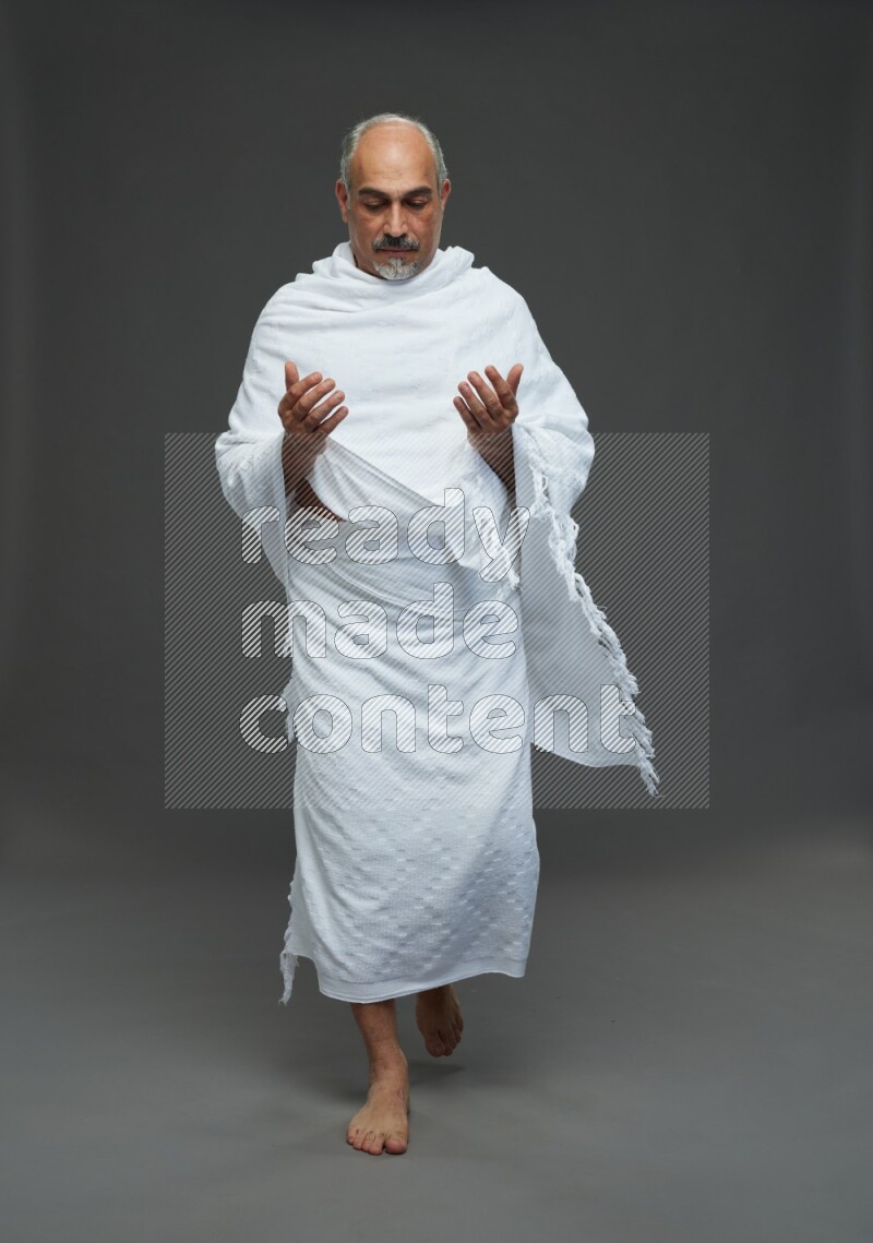 A man wearing Ehram Standing dua'a on gray background