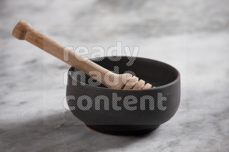 Black pottery bowl with wooden honey dipper in it on grey marble background