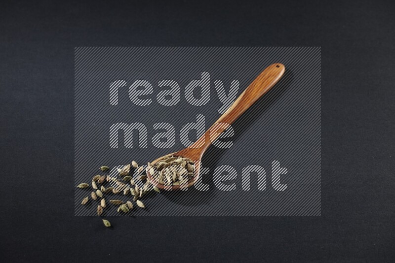 A wooden ladle full of cardamom on black flooring