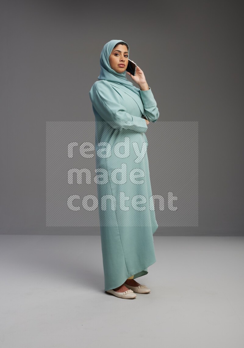 Saudi Woman wearing Abaya standing talking on phone on Gray background