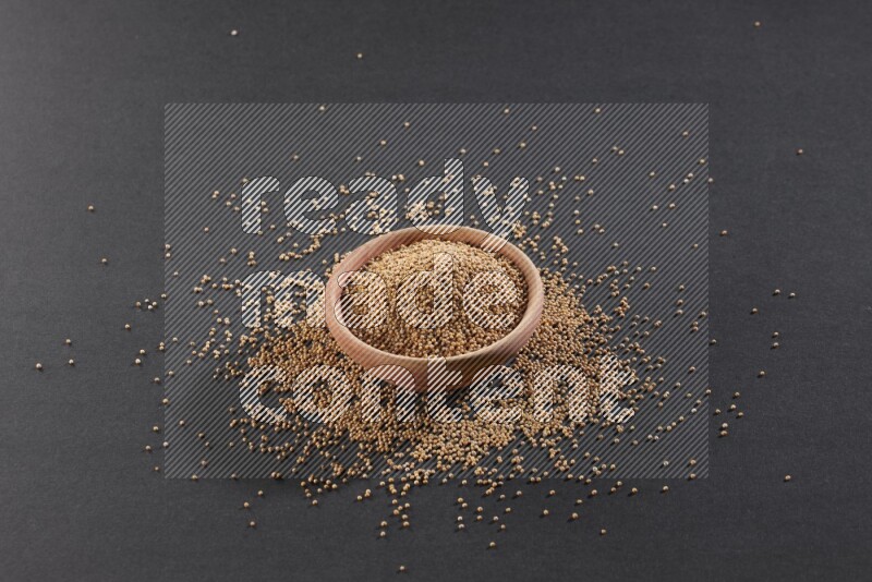 A wooden bowl full of mustard seeds and more seeds spread on a black flooring