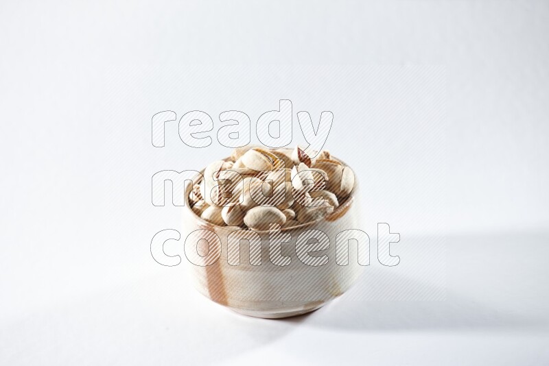 A beige ceramic bowl full of pistachios on a white background in different angles