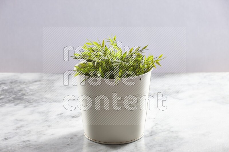 Green artificial plant in white pot on light grey marble background