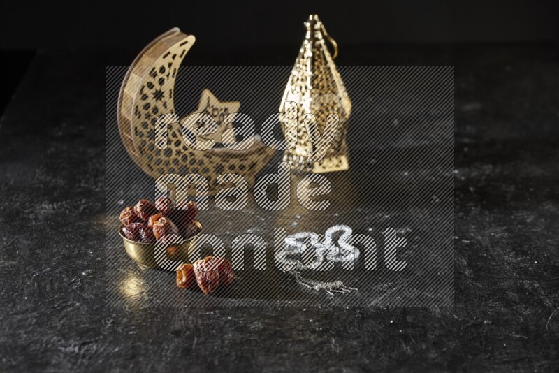 Dates in a metal bowl with prayer beads beside golden lanterns in a dark setup