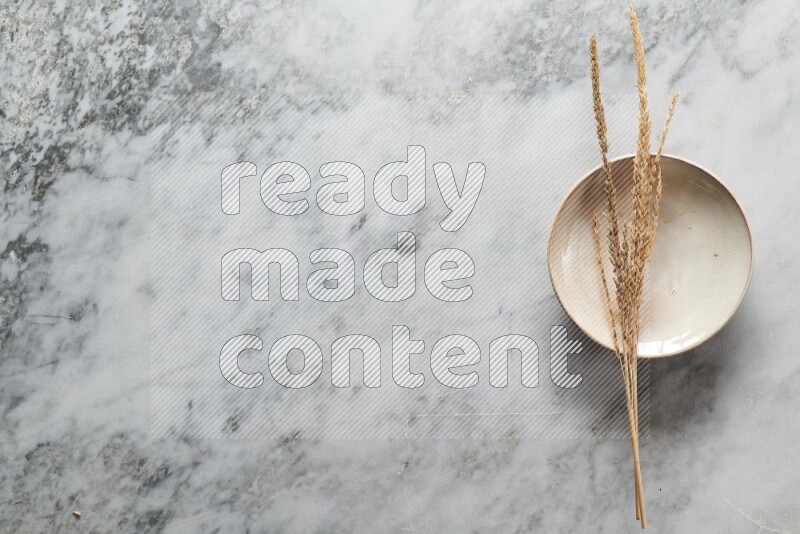 Wheat stalks on beige pottery plate on grey marble background