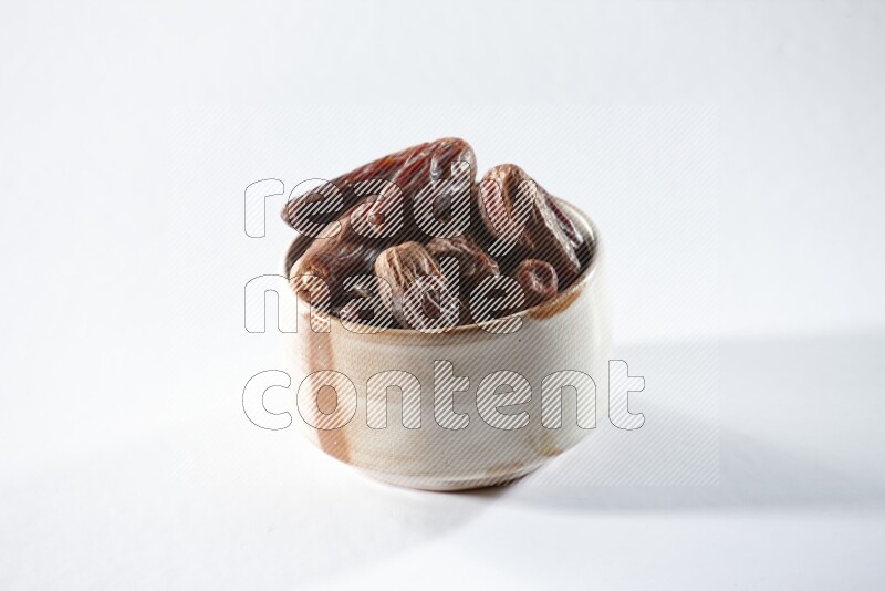 A beige ceramic bowl full of dried dates on a white background in different angles