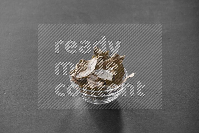 A glass bowl full of laurel leaves on black flooring