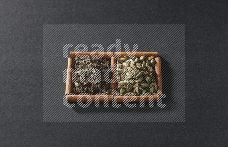 مربعان من أعواد القرفة ممتلئان بحبوب الهيل والريحان المجفف علي خلفية سوداء