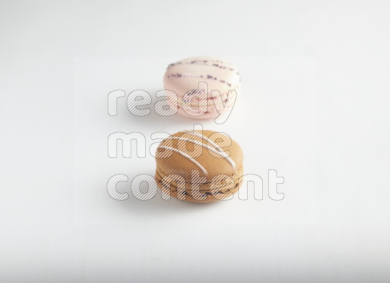 45º Shot of of two assorted Brown Irish Cream, and pink orange blossom macarons on white background