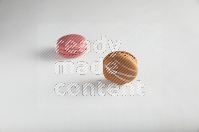 45º Shot of of two assorted Brown Irish Cream, and Pink Raspberry macarons on white background