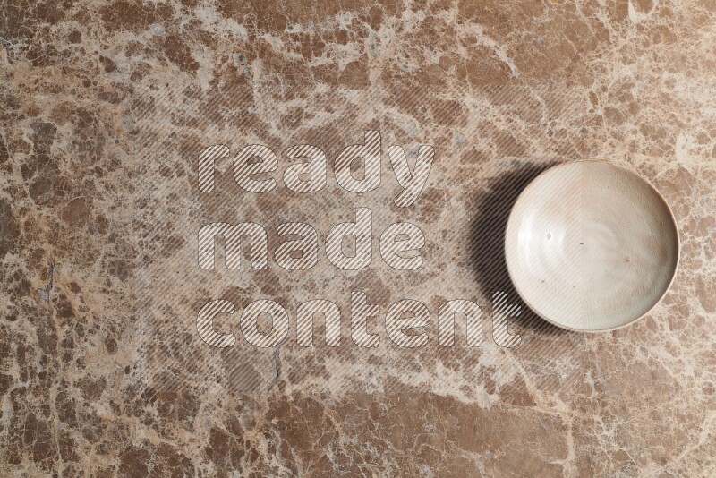 A beige pottery plate on beige marble background