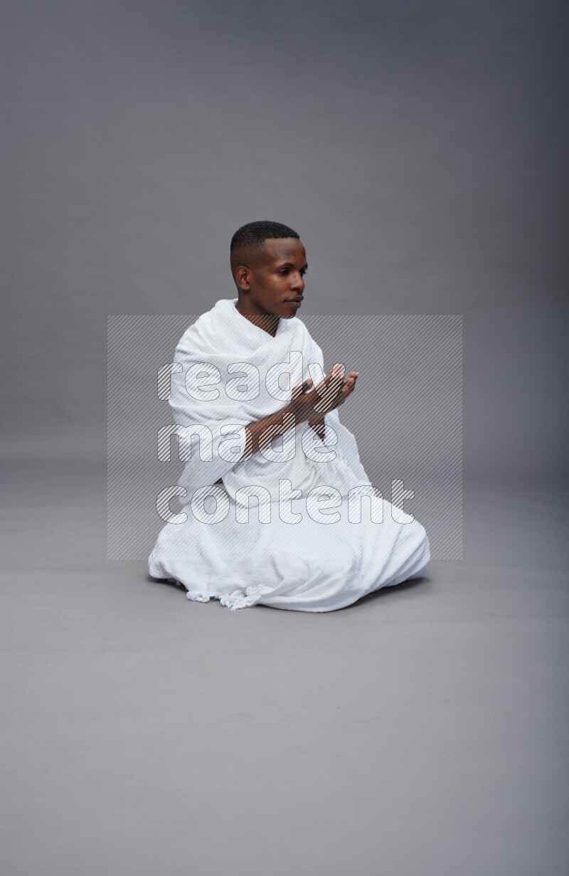 A man wearing Ehram sitting on floor dua'a on gray background