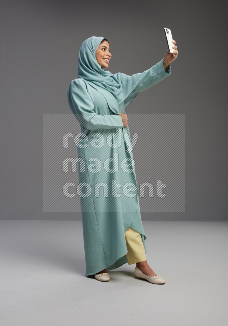 Saudi Woman wearing Abaya standing taking selfie on Gray background