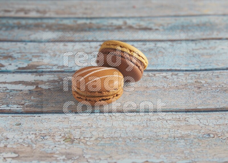 45º Shot of of two assorted Brown Irish Cream, and Yellow, and Brown Chai Latte macarons  on light blue background