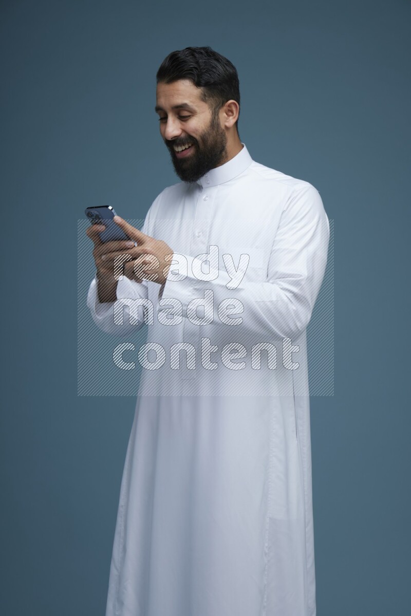 A man Texting in a blue background wearing Saudi Thob