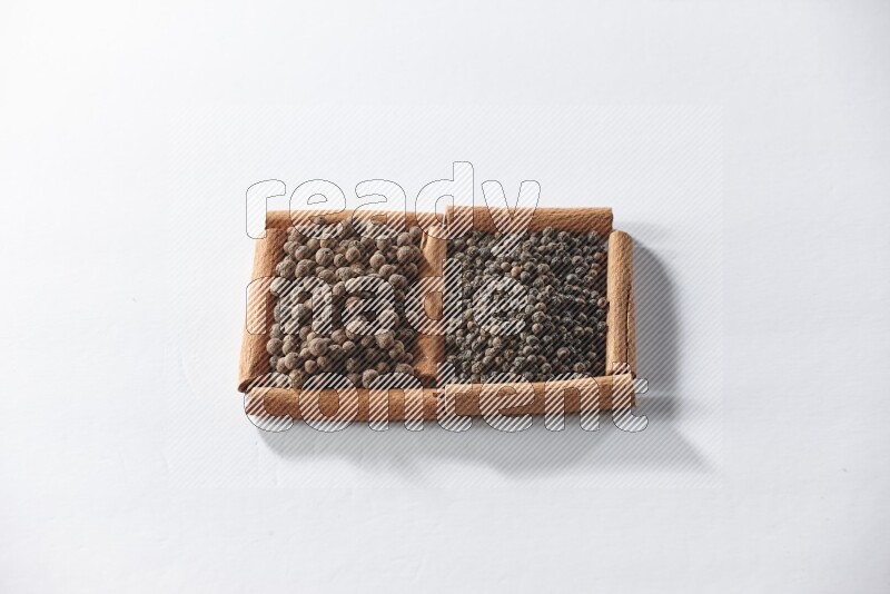 مربعان من أعواد القرفة ممتلئان بحبوب الفلفل الأسود وحبوب الفلفل الحلو علي خلفية بيضاء