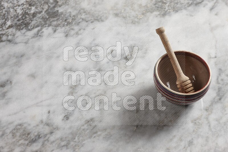 Multicolored pottery bowl with wooden honey dipper in it on grey marble background