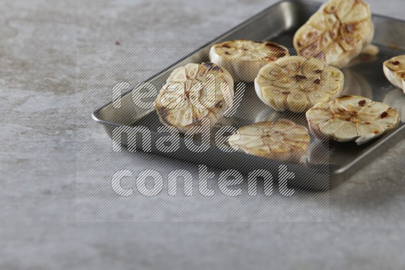 half's roasted garlic in a stainless tray on a grey textured countertop