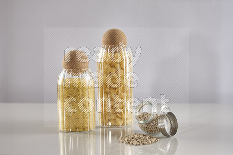 Raw pasta in glass jars with white peppers on light grey background