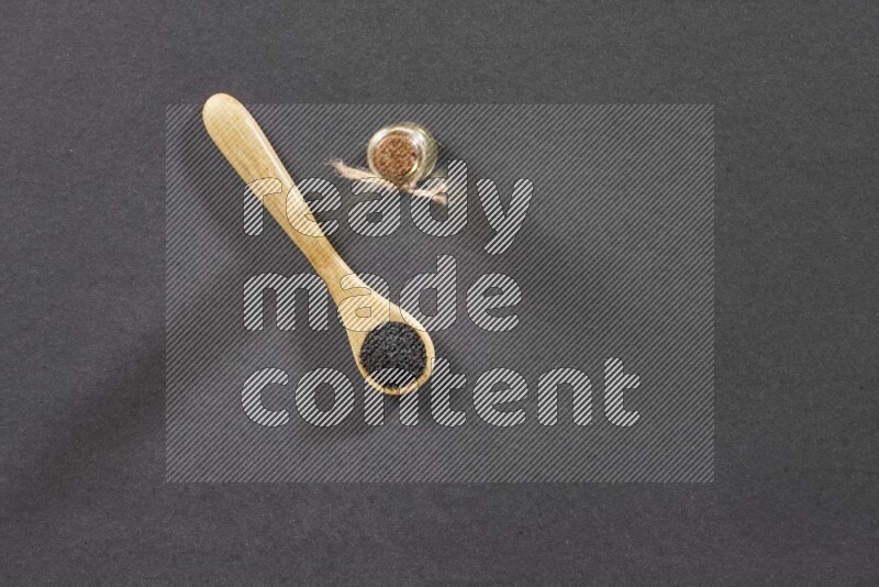 ملعقة خشبية ممتلئة بحبة البركة مع زجاجة من زيت حبة البركة على أرضية سوداء