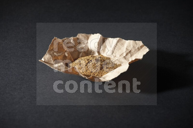 Cumin powder in a crumpled piece of paper on black flooring