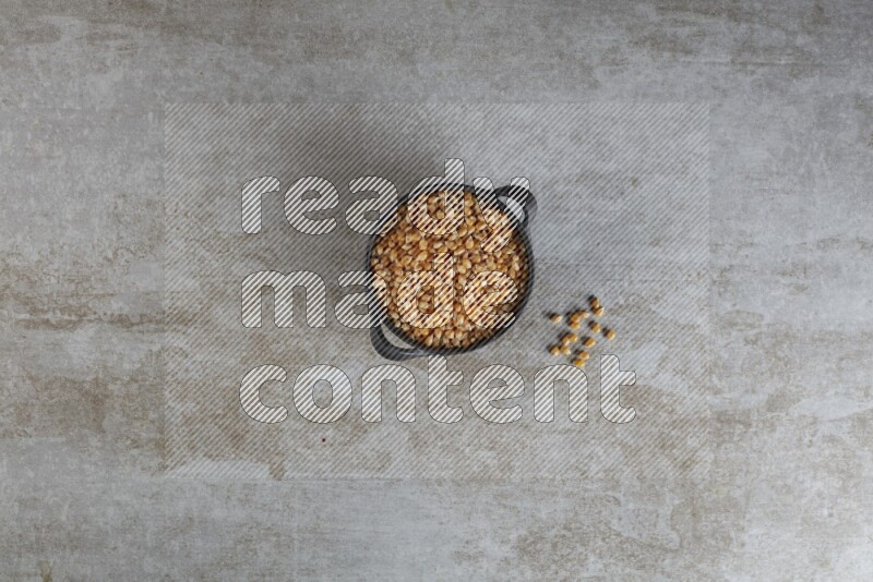 corn kernel in a black handheld ceramic bowl on a grey textured countertop