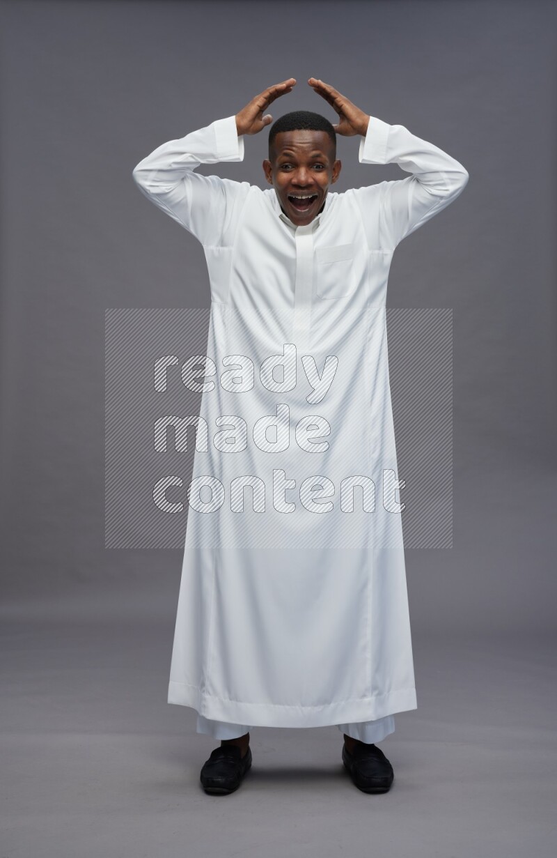 Saudi man wearing thob standing hands behind head on gray background