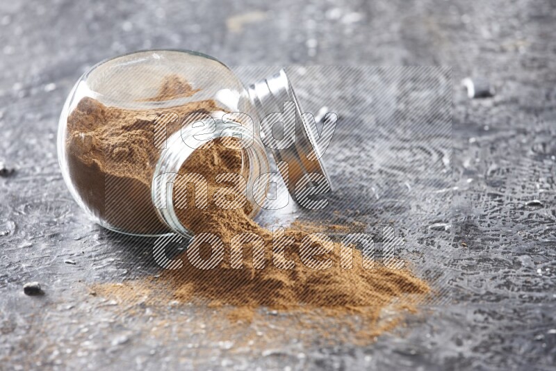 Flipped herbal glass jar full of cinnamon powder on textured black background