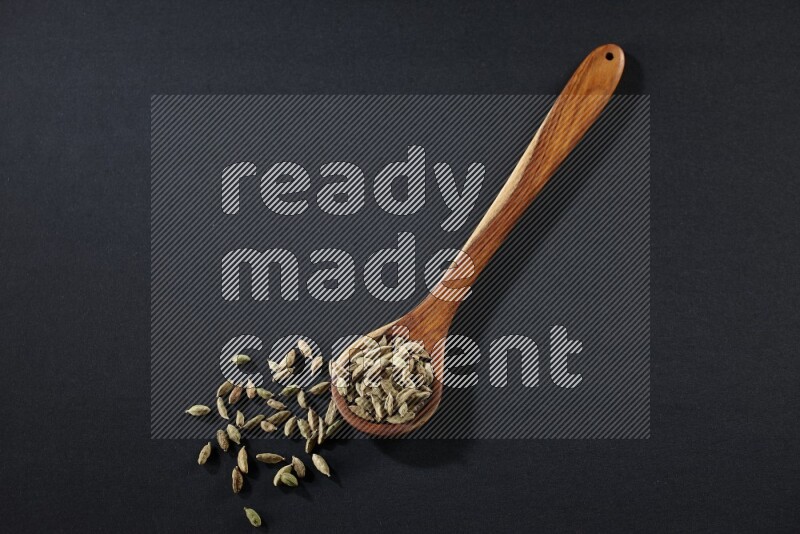 A wooden ladle full of cardamom on black flooring