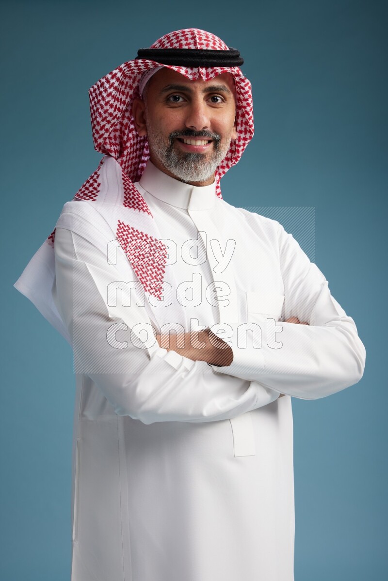 Saudi man wearing thob and shomagh posing to the camera on blue background
