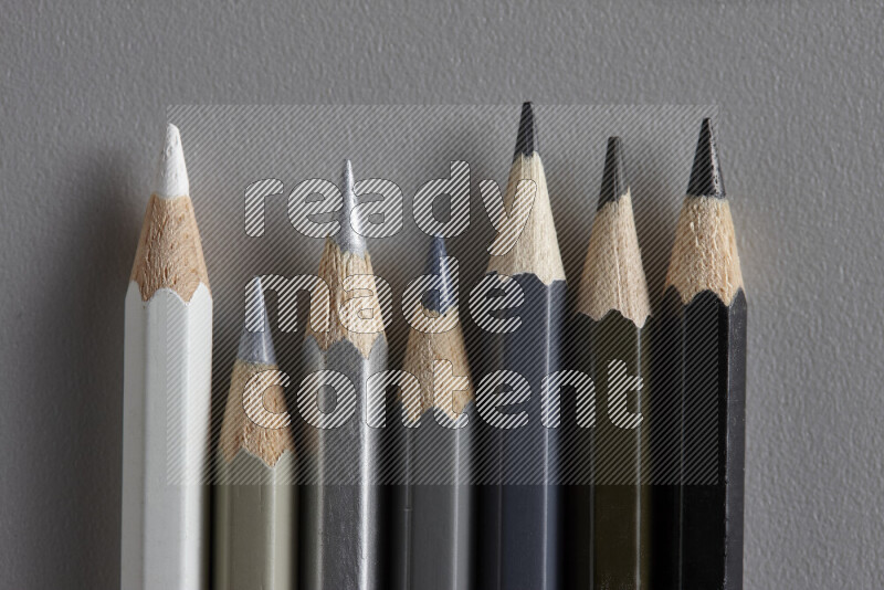 A collection of colored pencils arranged showcasing a gradient of white, grey and black hues on grey background
