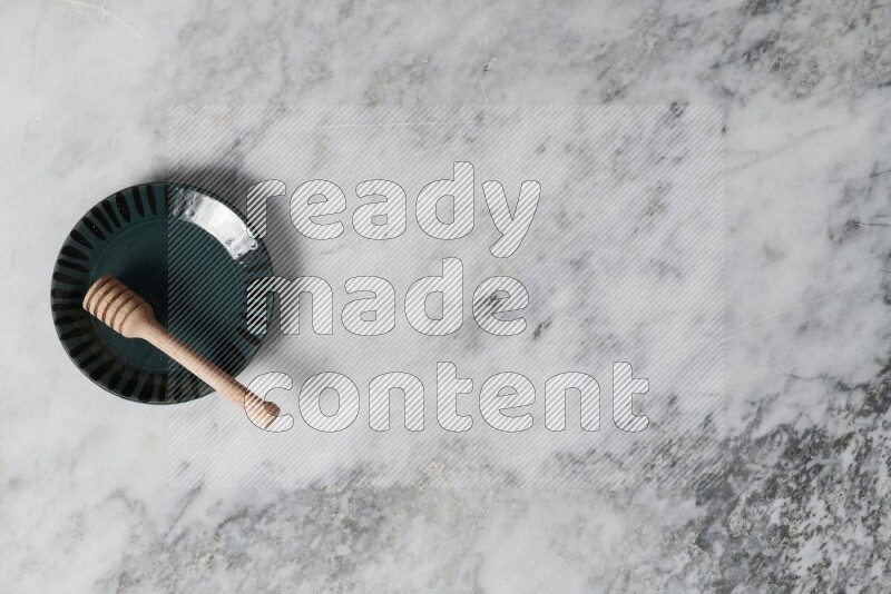 طبق فخاري متعدد الألوان مع ملعقة عسل خشبية بداخله على خلفية من الرخام الرمادي