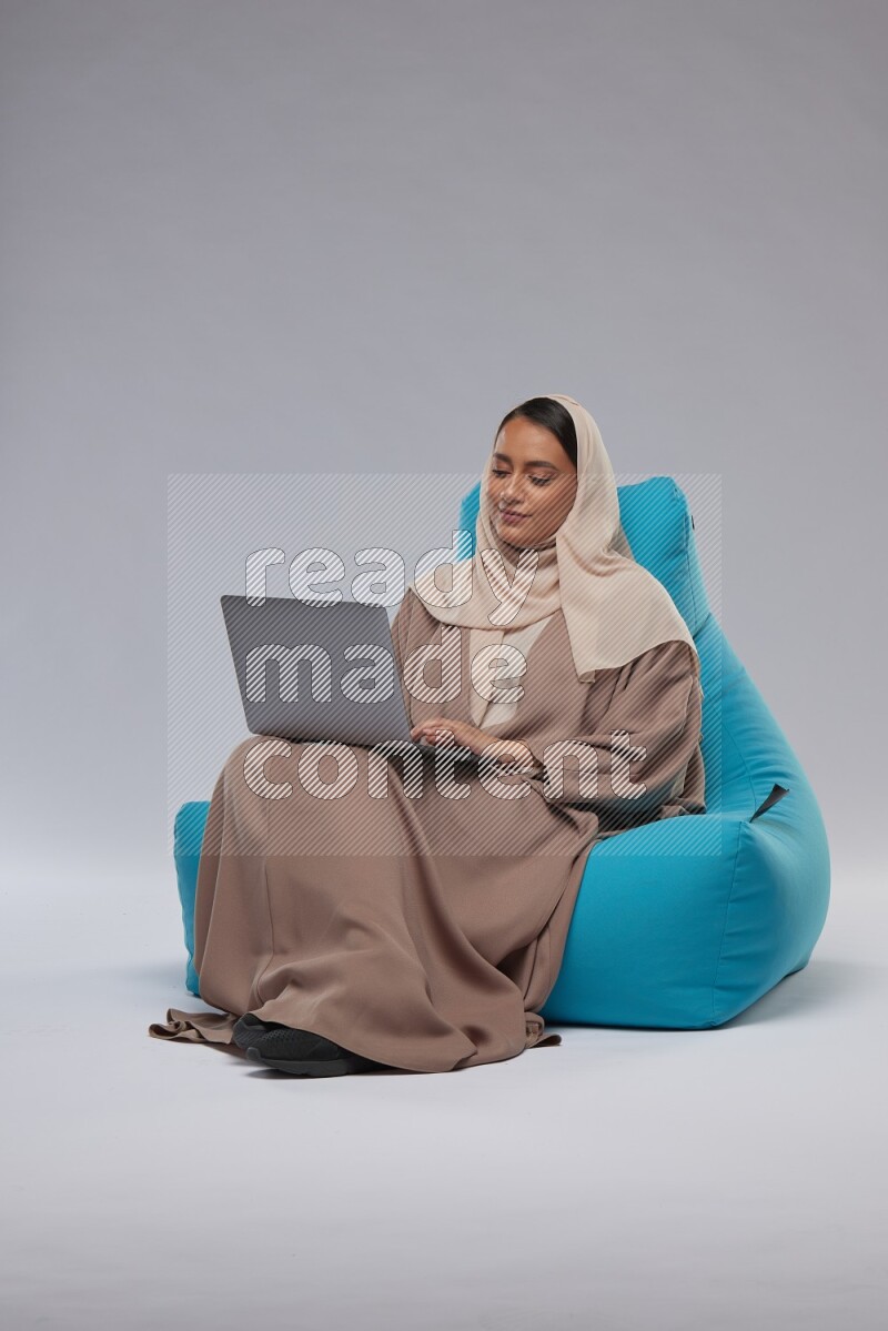 A Saudi woman sitting on a blue beanbag and working on laptop