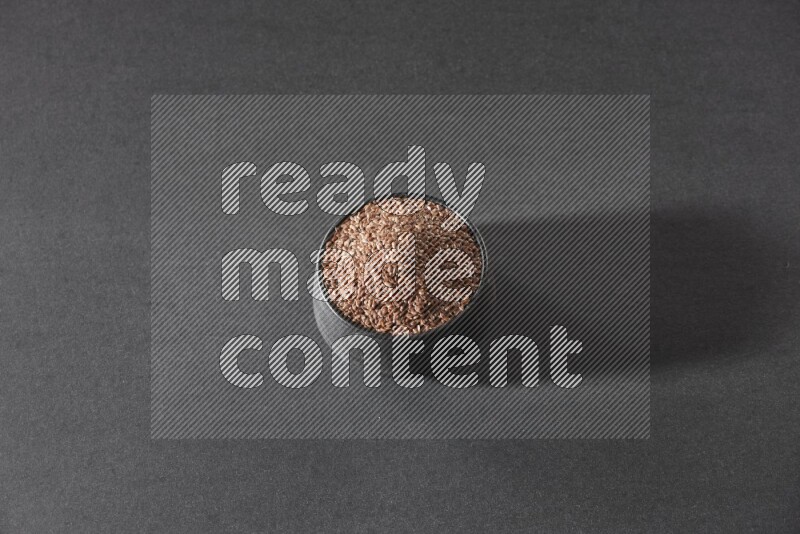 A black pottery bowl full of flaxseeds on a black flooring