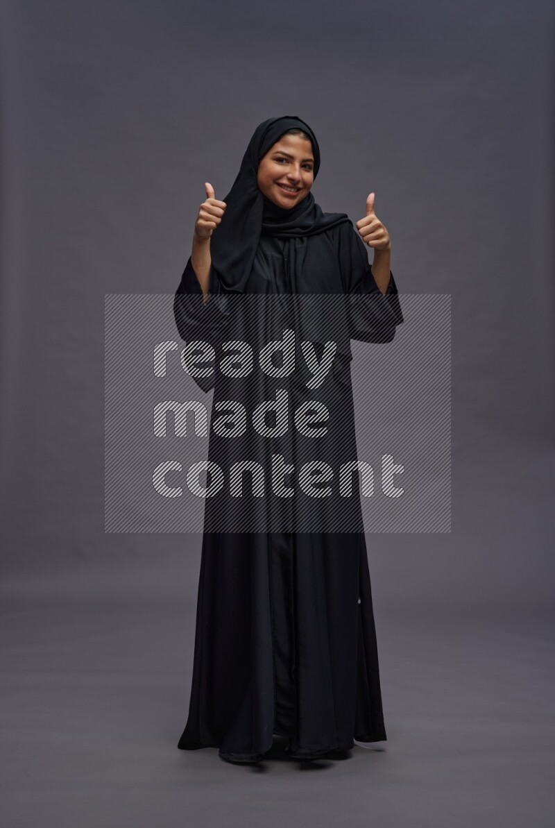 Saudi woman wearing Abaya standing interacting with the camera on gray background