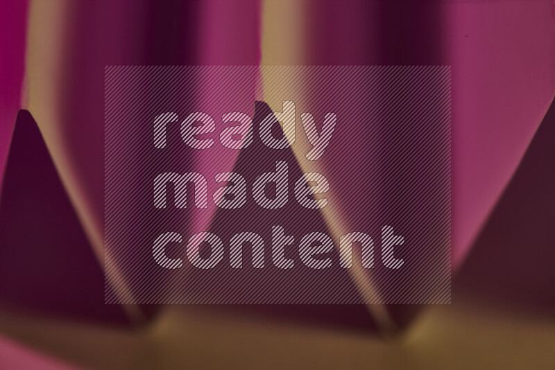 A close-up abstract image showing sharp geometric paper folds in pink gradients and warm tones