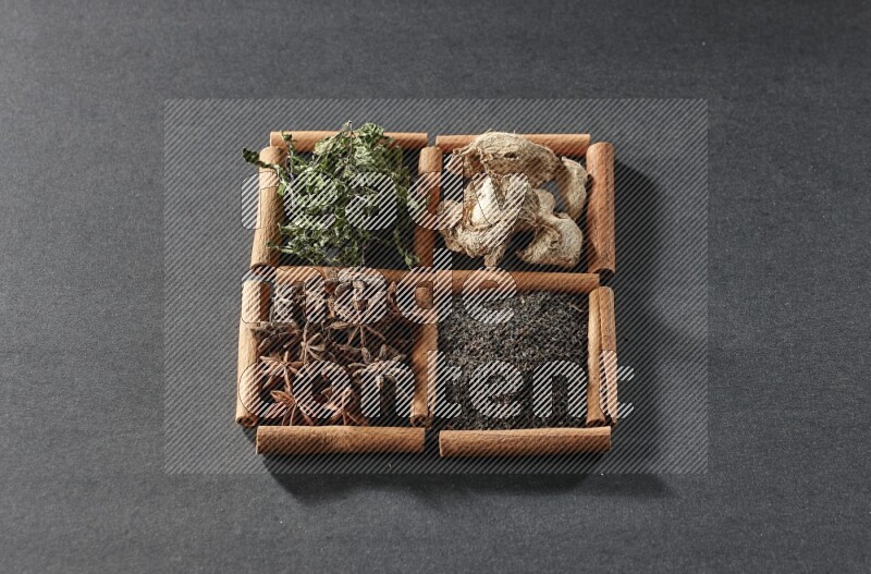 4 مربعات من عيدان القرفة ممتلئة بالشاي الأسود والزنجبيل المجفف والنعناع المجفف واليانسون النجمي على أرضية سوداء