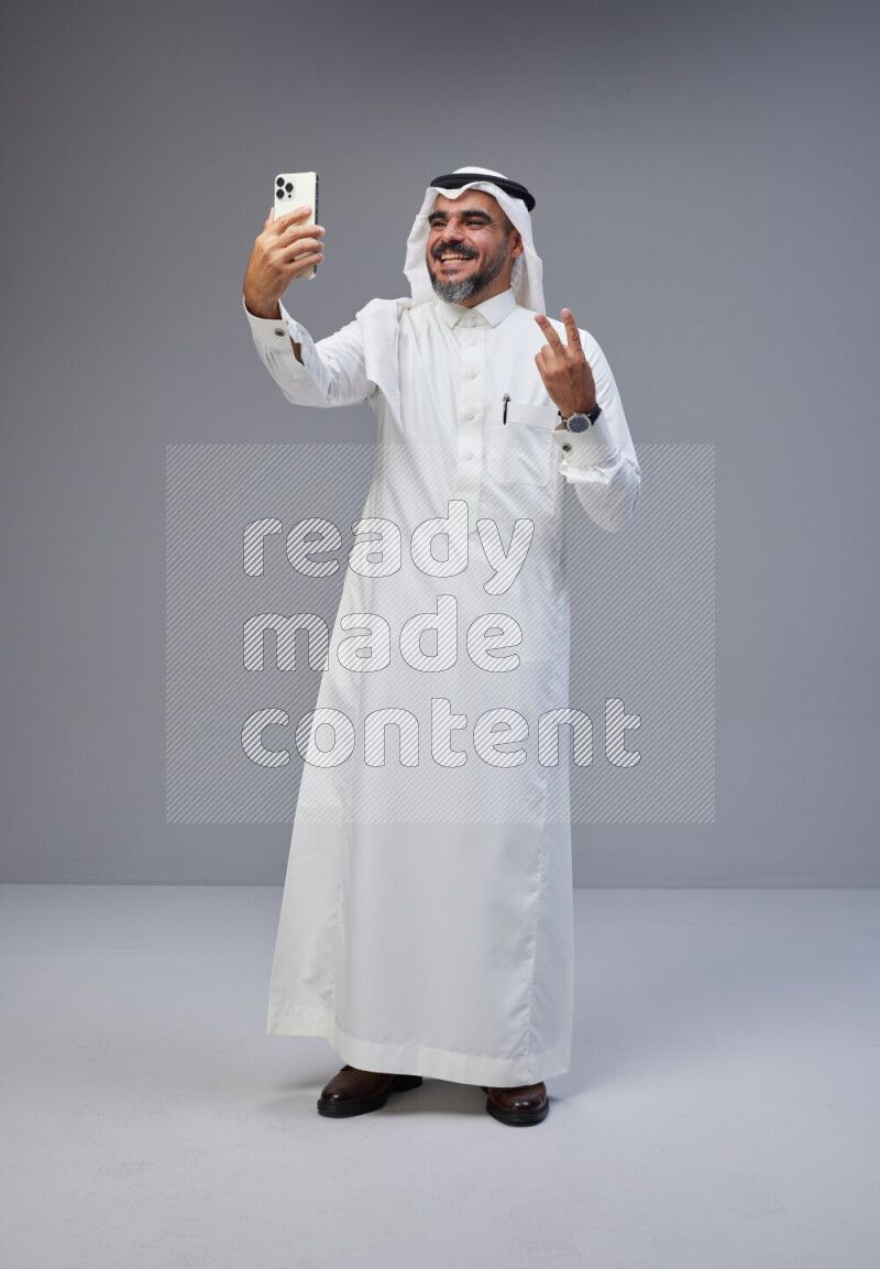 Saudi man Wearing Thob and white Shomag standing taking selfie on Gray background